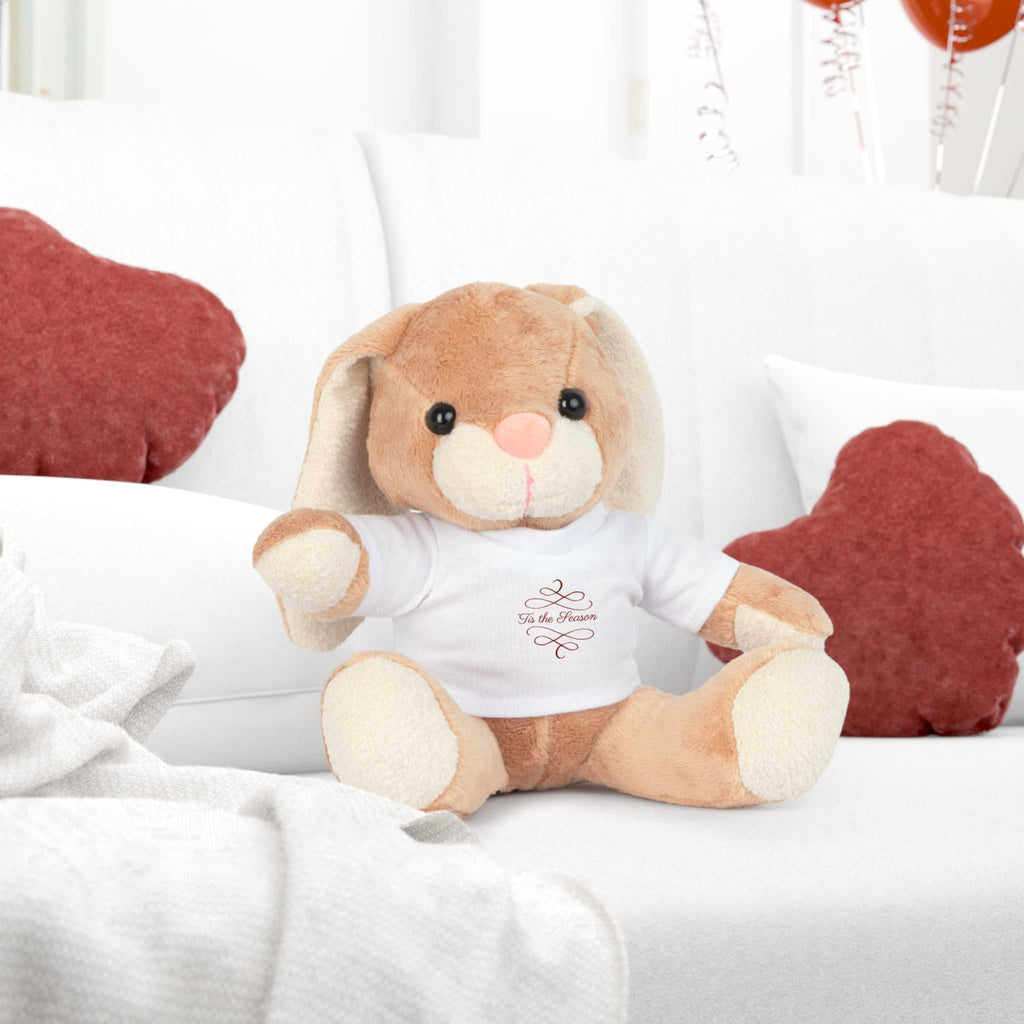 Tis the Season brown teddy plush toy wearing holiday t-shirt on white couch with red pillows