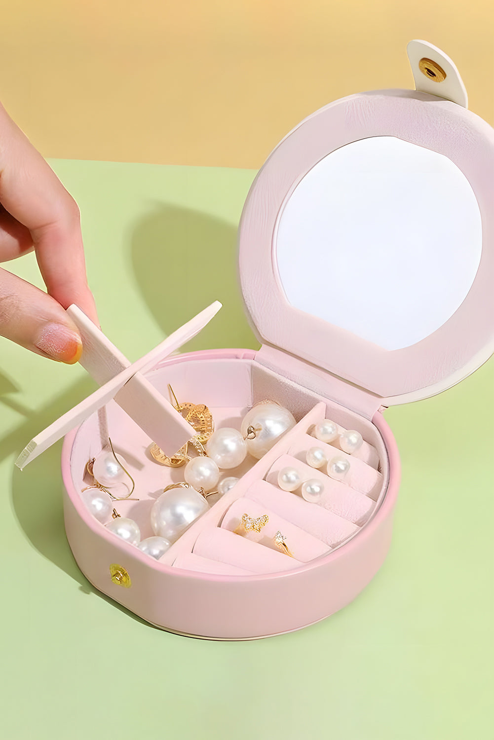 Light pink jewelry organizer case with snap closure and built-in mirror, compact and round-shaped for easy carrying